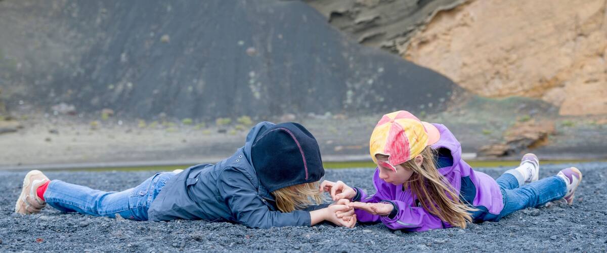 Two people lying on a beach with rocky cliffs in the background.
