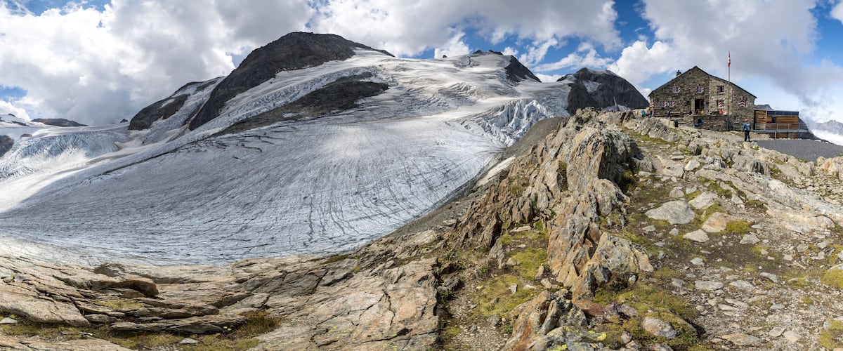 A glacier with a stone building on a rocky outcrop.