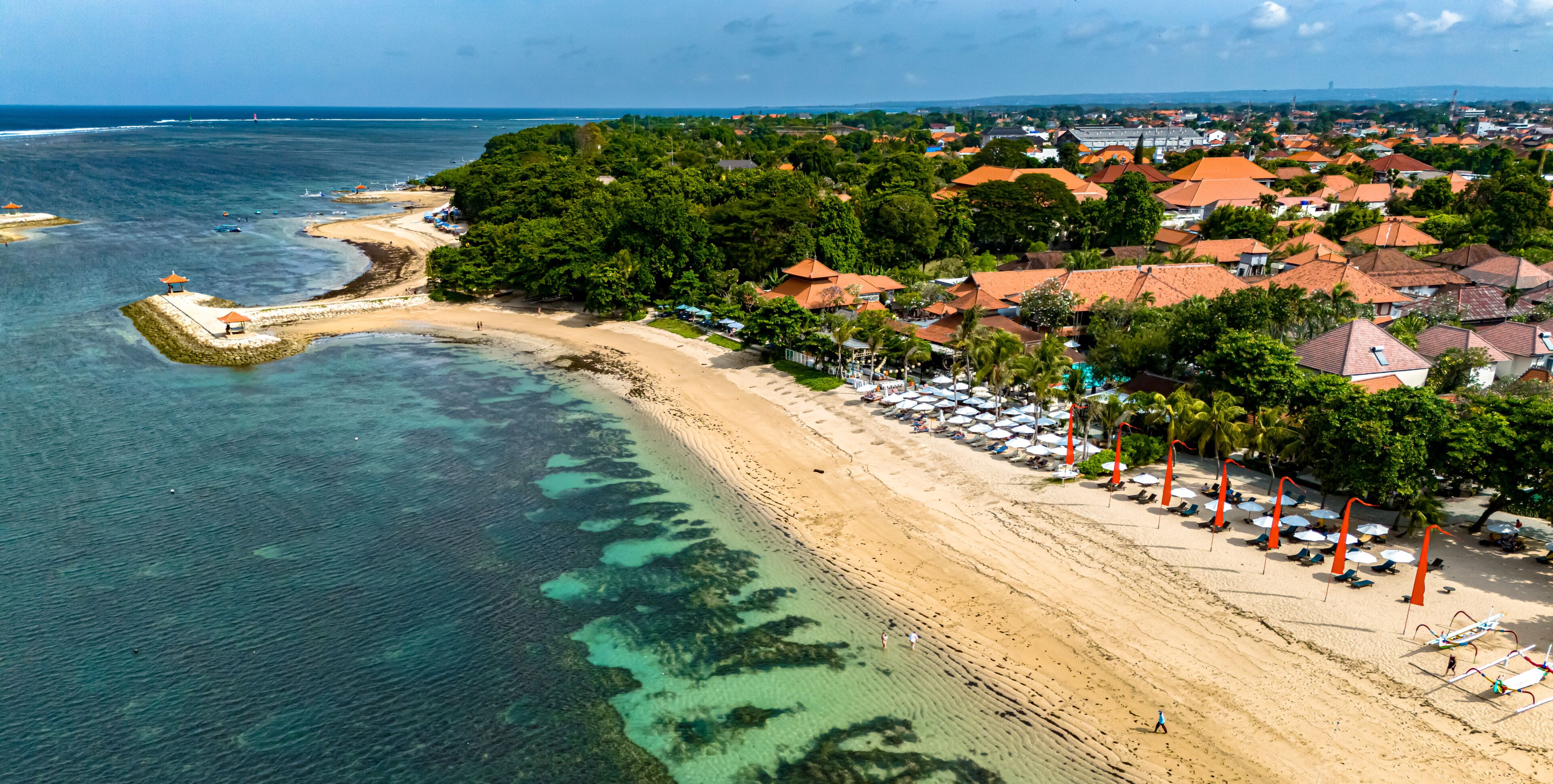 A coastal town with a beach, clear waters, and red-roofed houses.