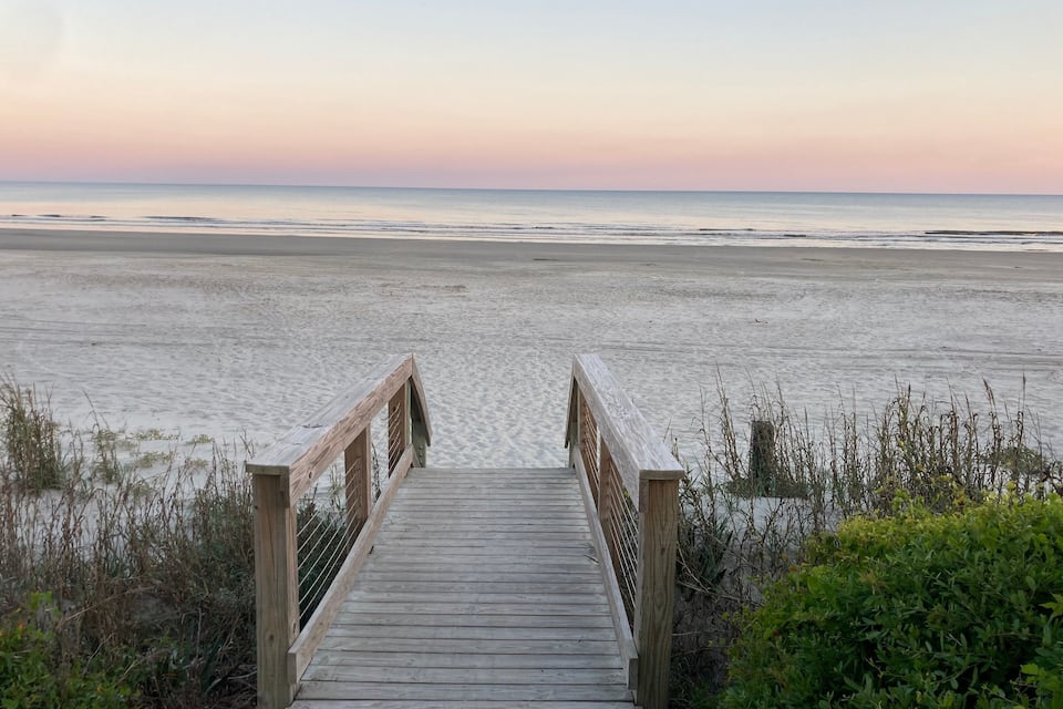 A wooden boardwalk leading to a beach with a calm sea and a sunset sky.