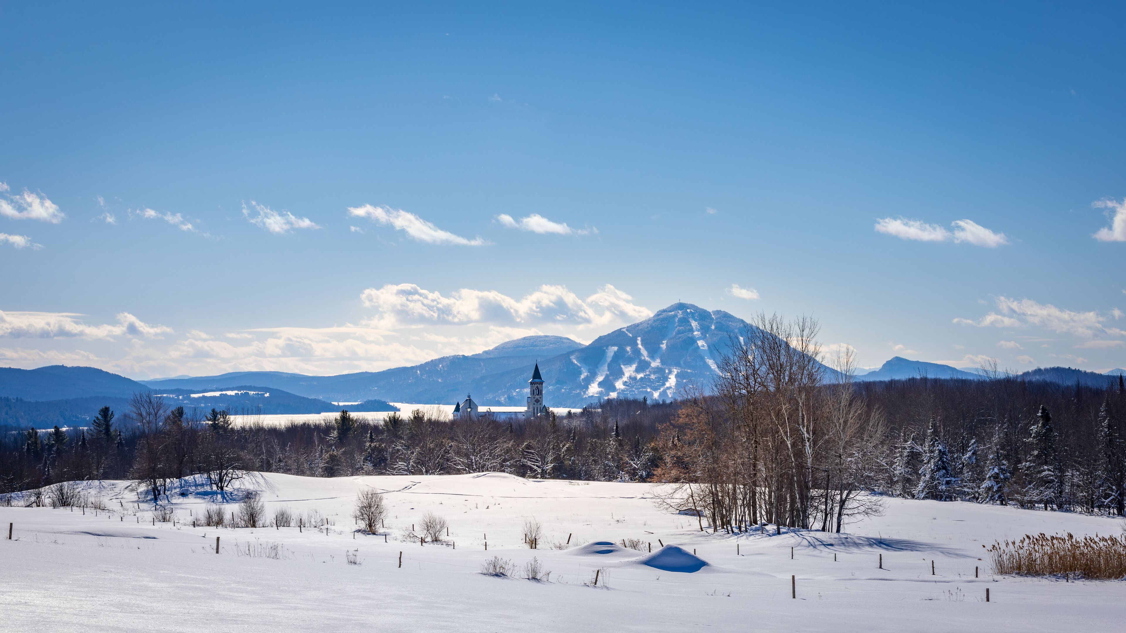 A snow-covered landscape with a church, mountains, and a clear sky.