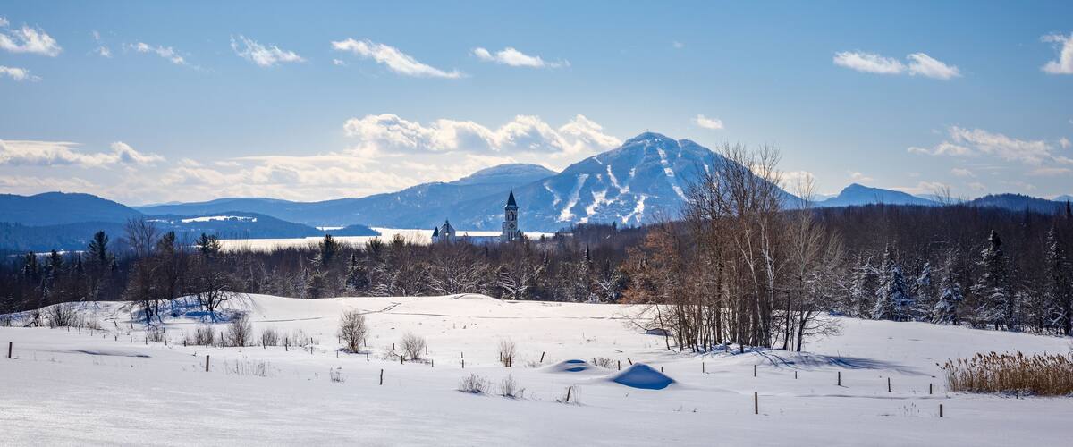 A snow-covered landscape with a church, mountains, and a clear sky.