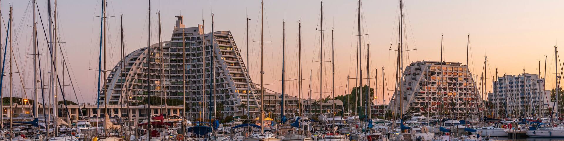 A marina with numerous sailboats docked in front of modern buildings.