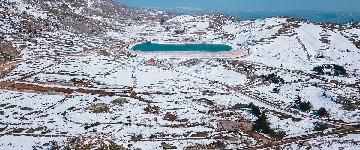 A snow-covered landscape with a large turquoise lake surrounded by mountains.