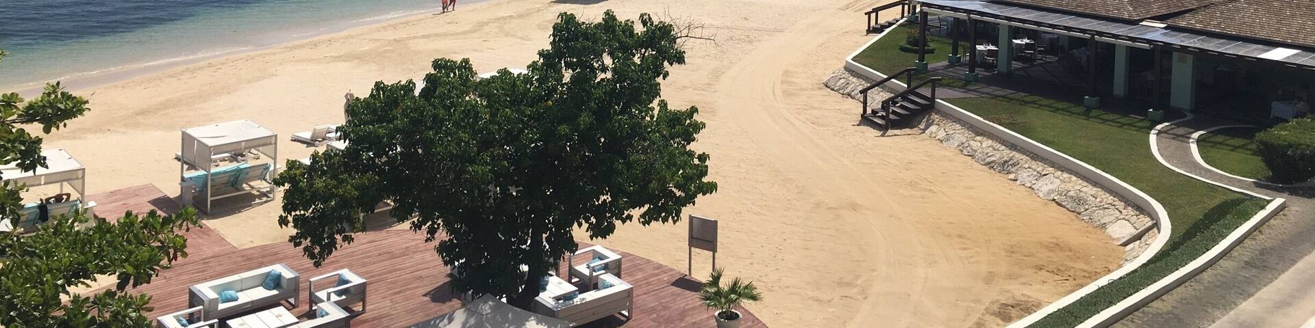 A beach with a lifeguard tower, lounge chairs, and a building with a tiled roof.