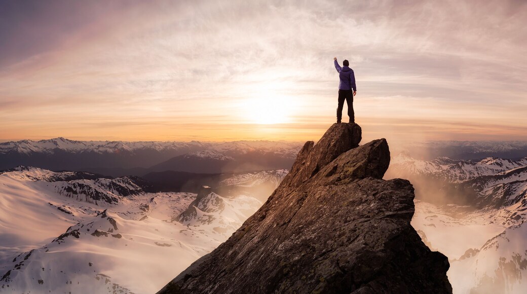 Magical Fantasy Adventure Composite of Man Hiking on top of a rocky mountain peak. Background Landscape from British Columbia, Canada. Sunset or Sunrise Colorful Sky