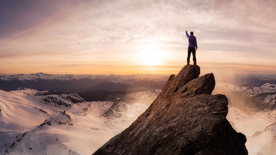 Magical Fantasy Adventure Composite of Man Hiking on top of a rocky mountain peak. Background Landscape from British Columbia, Canada. Sunset or Sunrise Colorful Sky