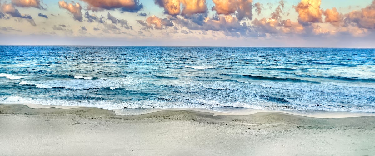 A beach with waves and a sky with clouds.