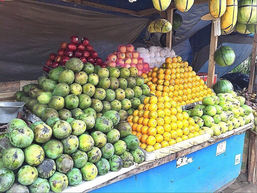 A fruit stand with various fruits including guavas, oranges, and apples.