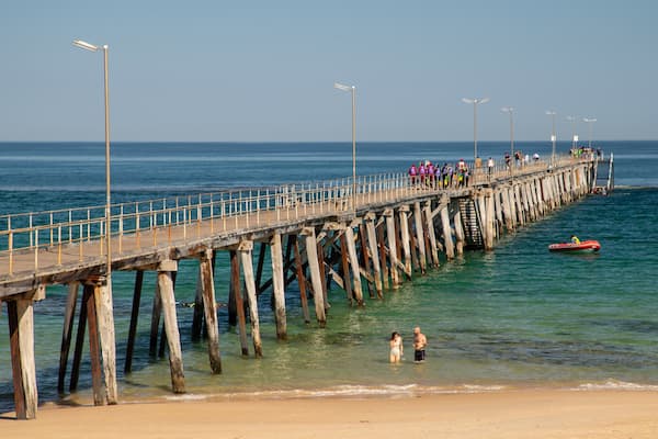 Um píer de madeira se estende até o oceano, com pessoas caminhando.