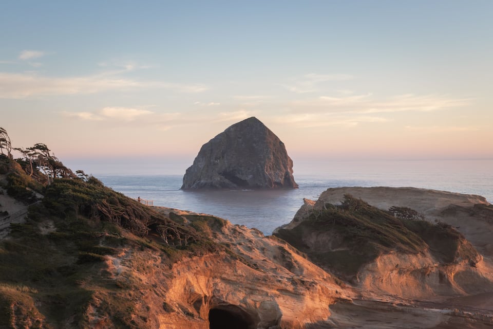 Una costa rocciosa con una formazione rocciosa imponente al centro, circondata da scogliere erbose e l'oceano.