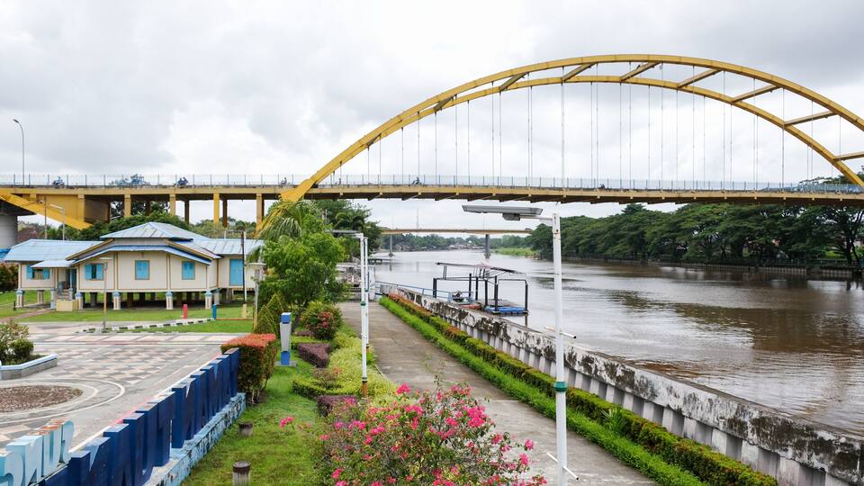 A yellow bridge over a river, a blue building, and a pathway with pink flowers.