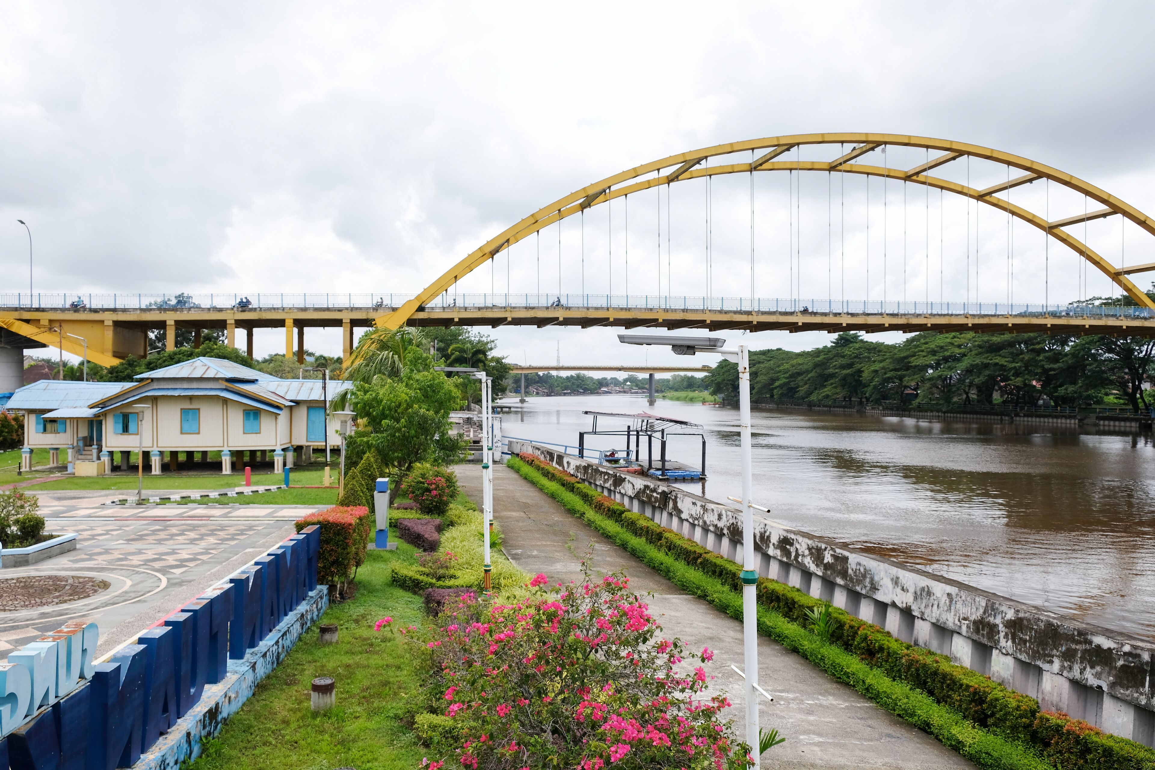 A yellow bridge over a river, a blue building, and a pathway with pink flowers.