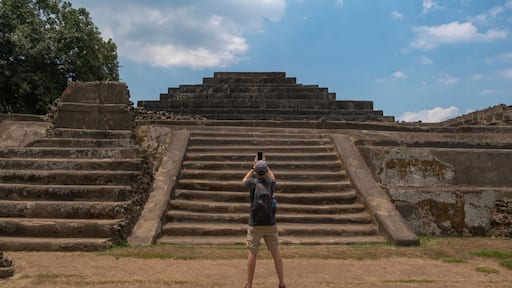 Young man tourist taking photos with the phone at the main pyramid with temple at Tazumal Park archaeological site in El Salvador.
