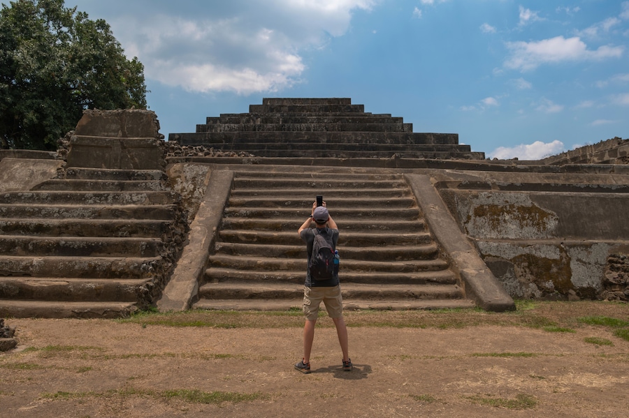 Young man tourist taking photos with the phone at the main pyramid with temple at Tazumal Park archaeological site in El Salvador.