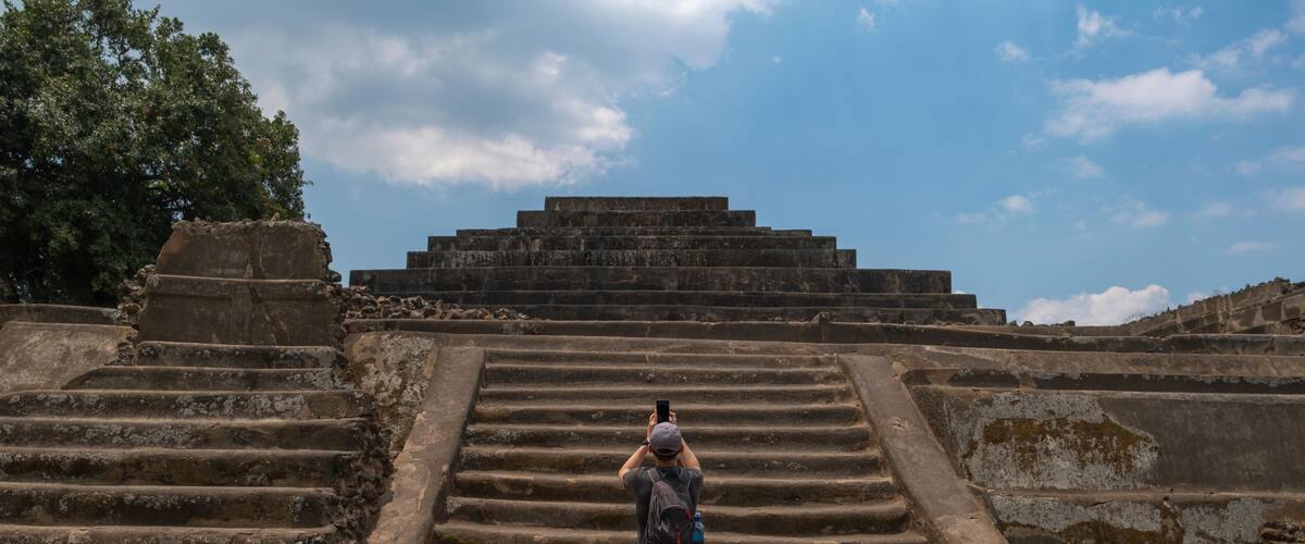 A person taking a photo of ancient stone steps leading to a pyramid.