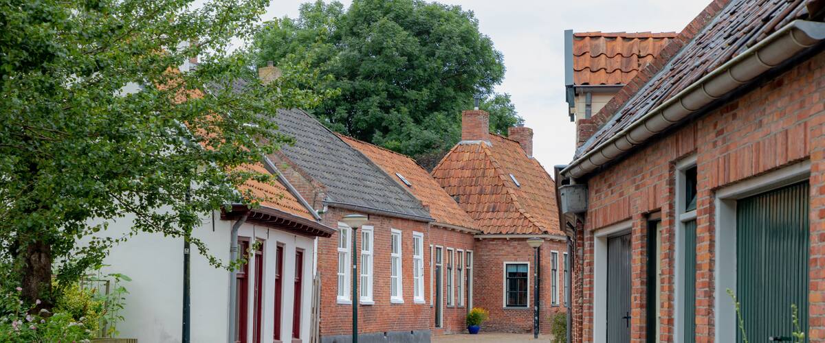 A narrow cobblestone street lined with traditional brick buildings, some with green shutters and red doors.