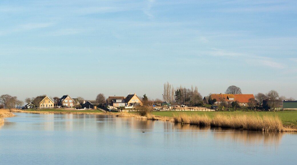 A river with houses along its banks, a clear sky, and a calm water surface reflecting the surroundings.