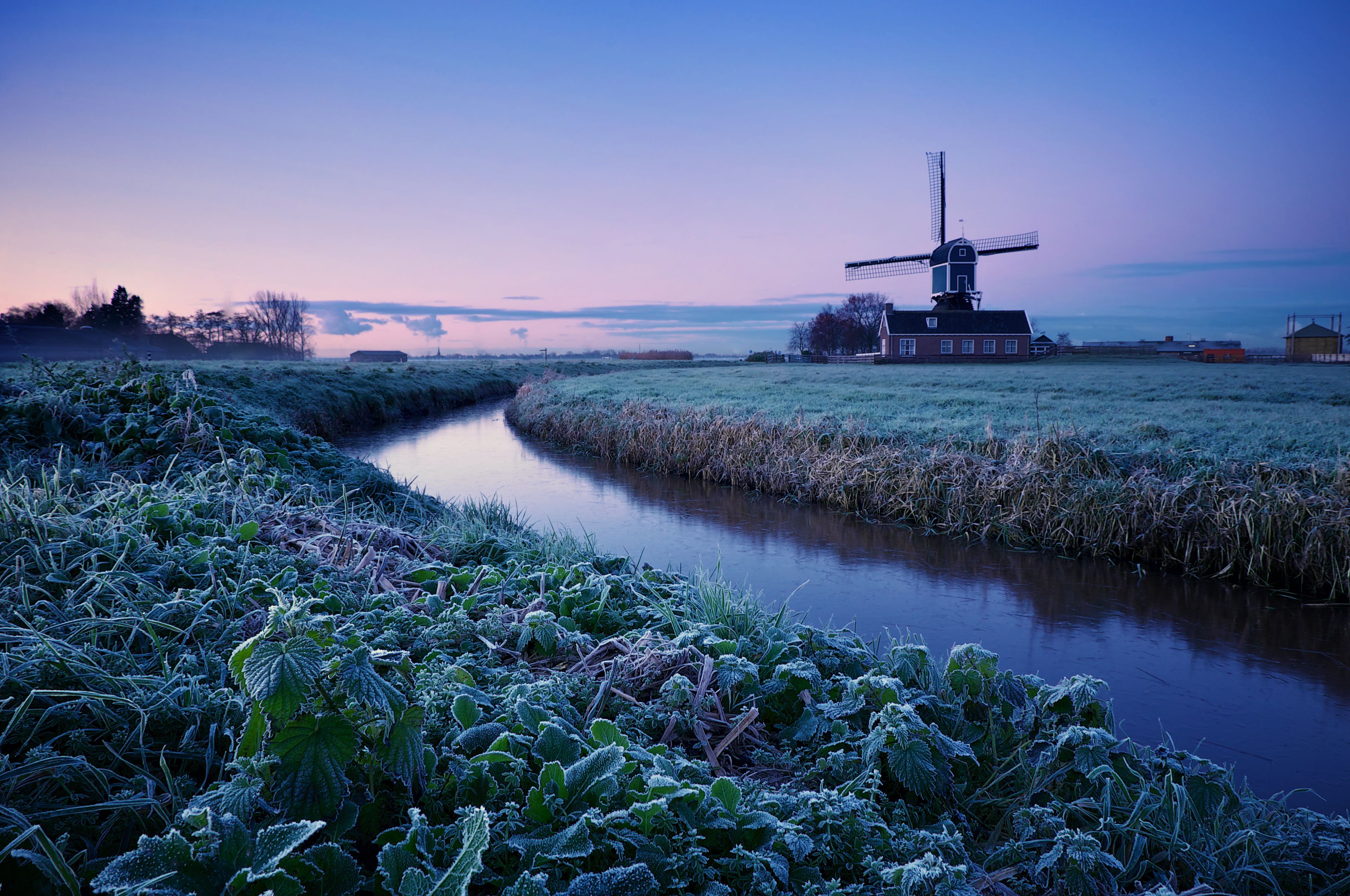 A frost-covered canal with a windmill and a red building in the background.