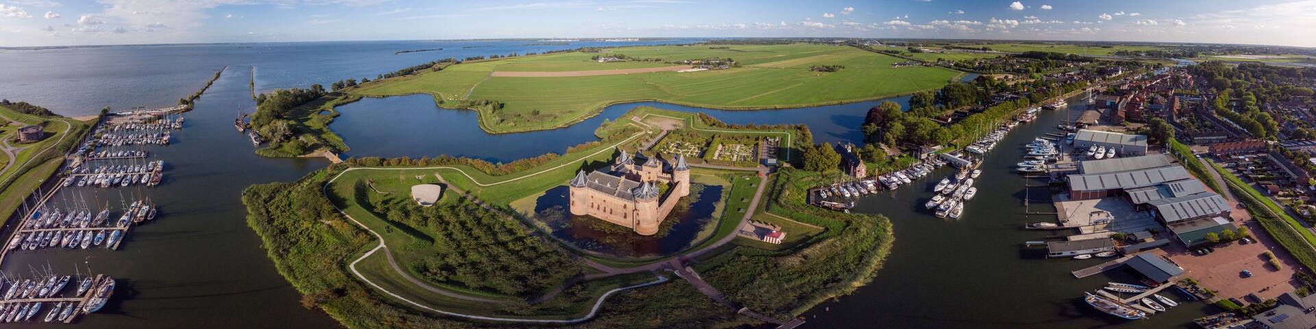 Wide aerial panoramic view of the Muiderslot castle in Muiden near Amsterdam and its lush gardens at the IJsselmeer with surrounding water entrenchment and port area and harbour of the historic city