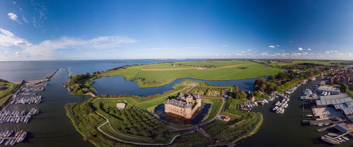 A castle surrounded by a moat, a golf course, and a marina with boats.