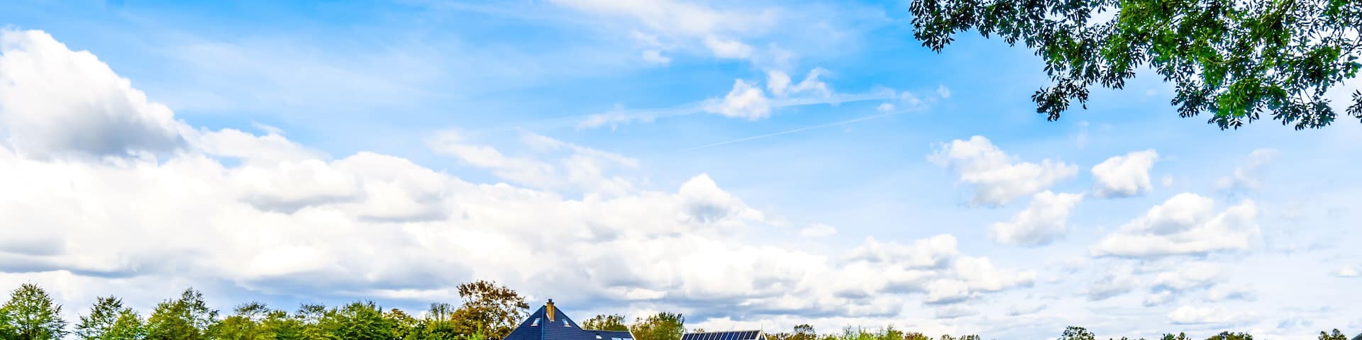 A rural landscape with a green field, a small pond, and houses with solar panels.