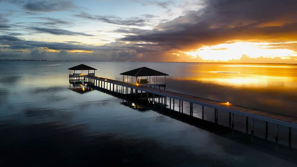 A pier extending into calm waters with two covered structures at the end.