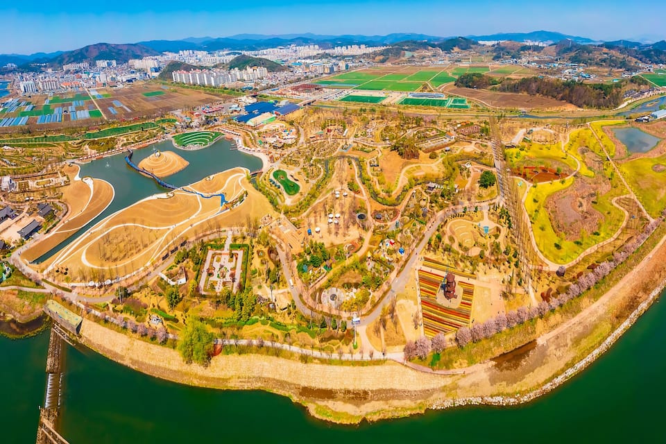 An aerial view of a city with a river, green fields, and a bridge.