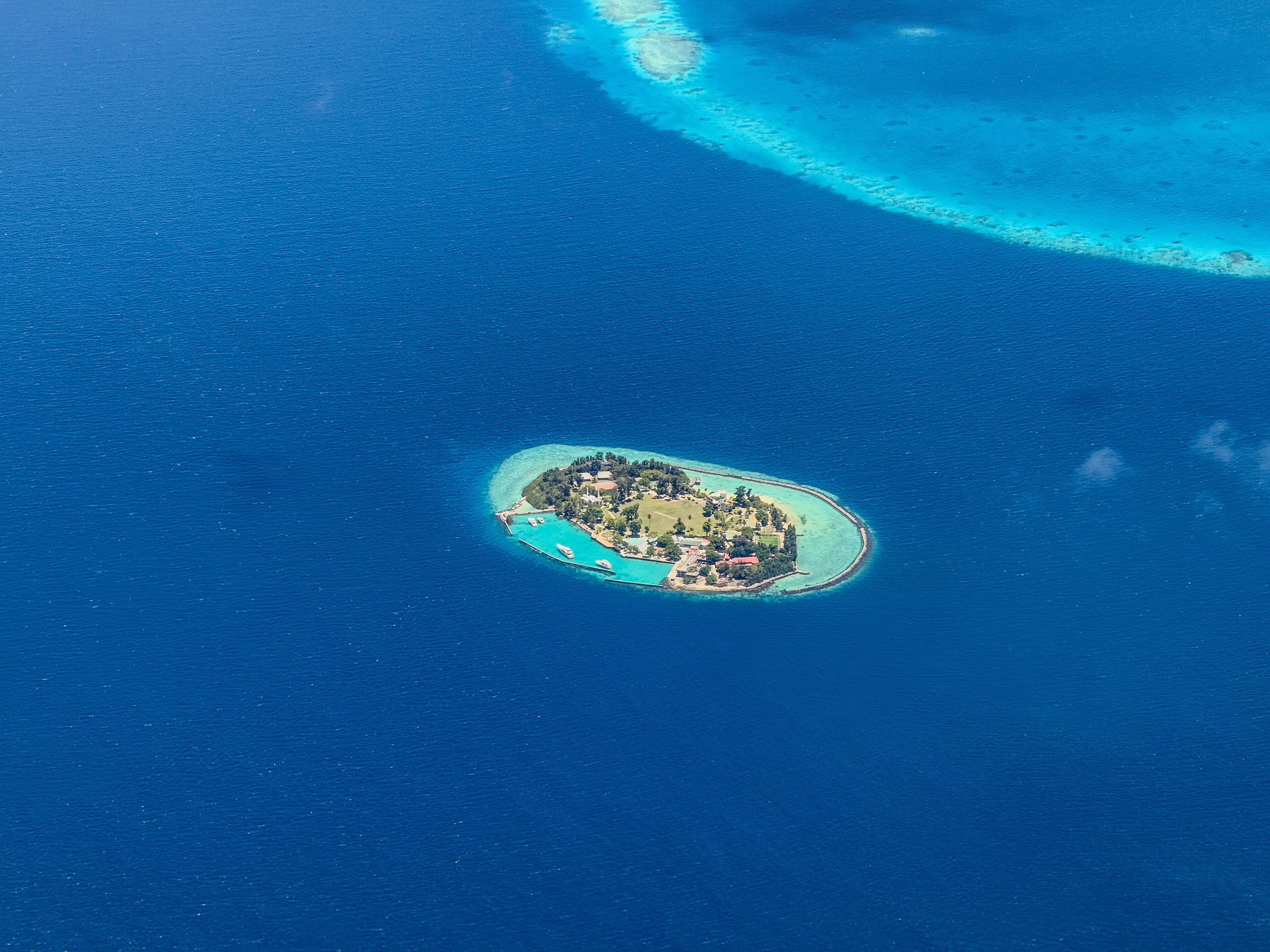 An aerial view of a small island with a dense cluster of buildings surrounded by clear blue waters and a coral reef.
