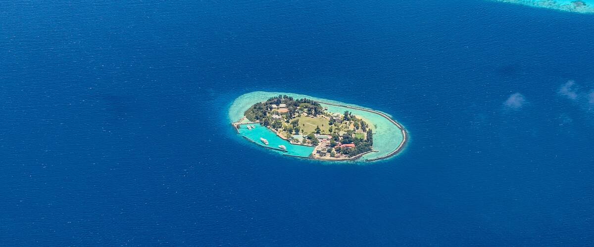 An aerial view of a small island with a dense cluster of buildings surrounded by clear blue waters and a coral reef.