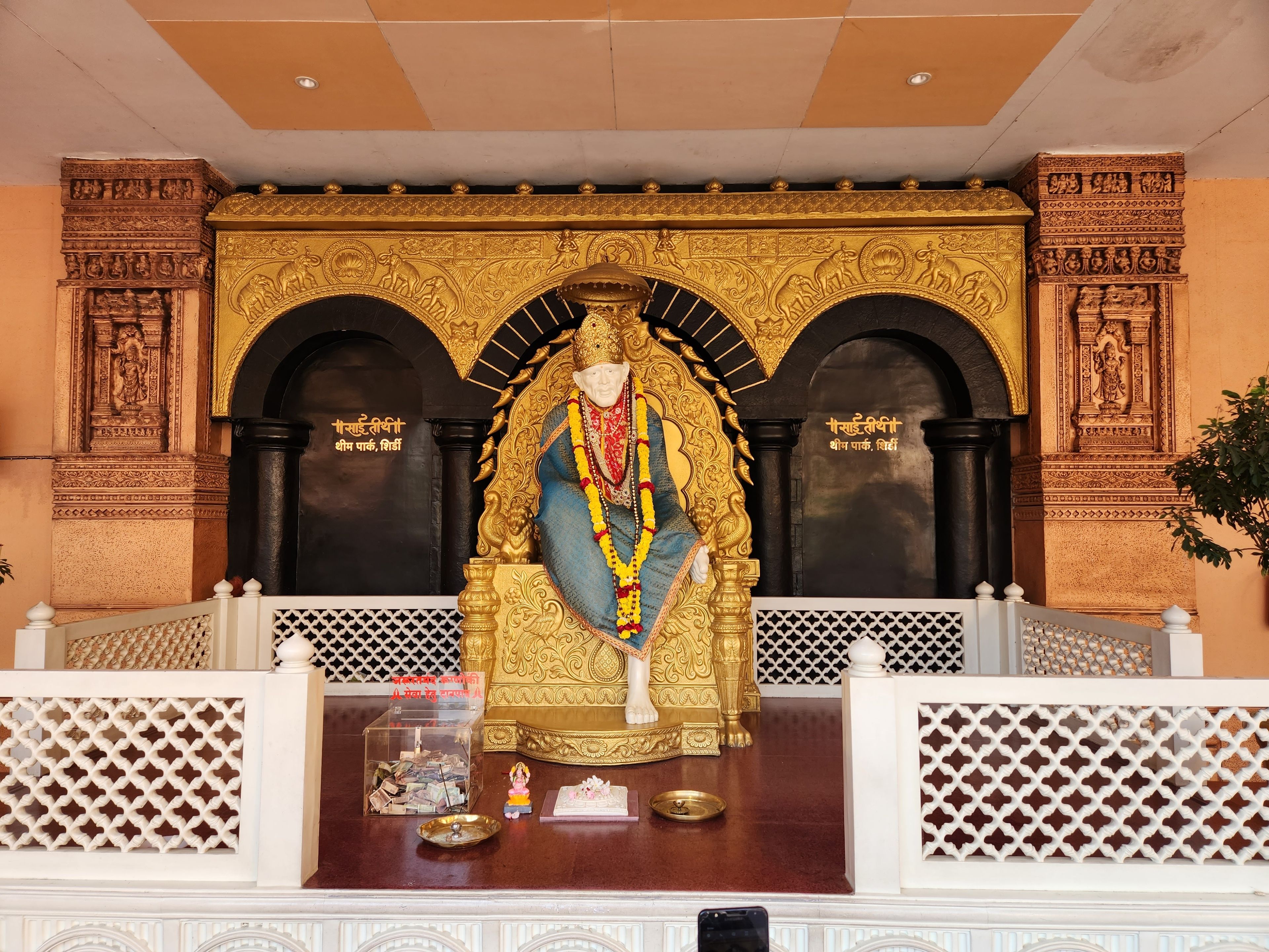 A statue of a deity with intricate golden decorations, a black background, and a white lattice railing in front.