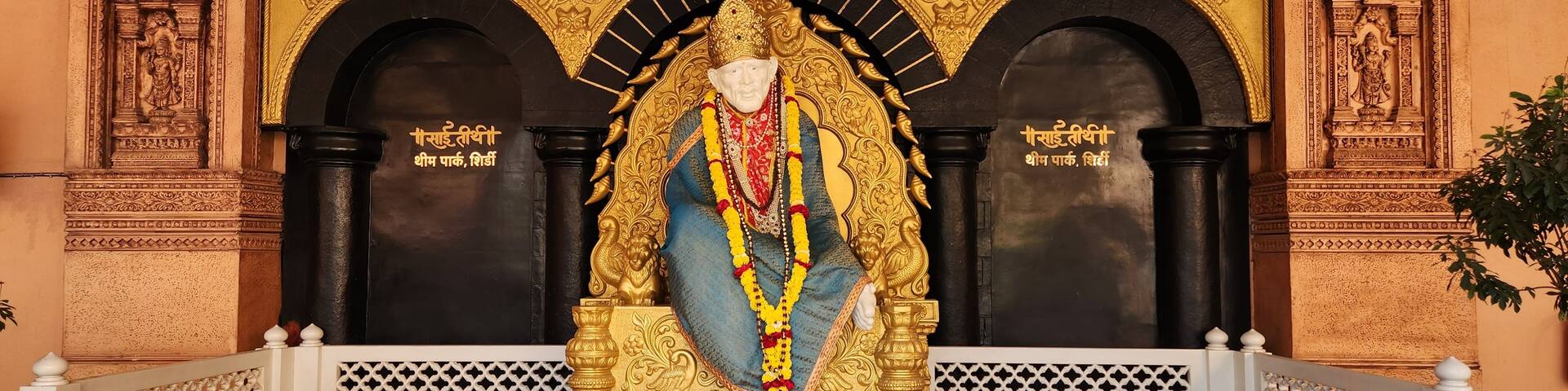 A statue of a deity with intricate golden decorations, a black background, and a white lattice railing in front.