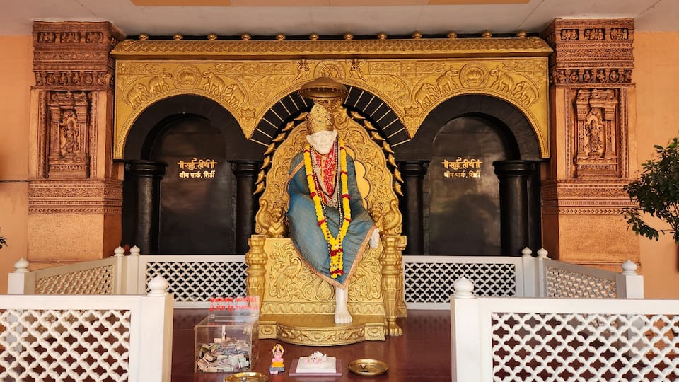 A statue of a deity with intricate golden decorations, a black background, and a white lattice railing in front.