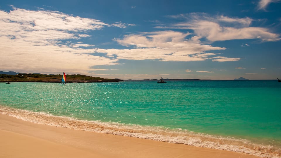 A beach with turquoise water, a sailboat, and distant land.