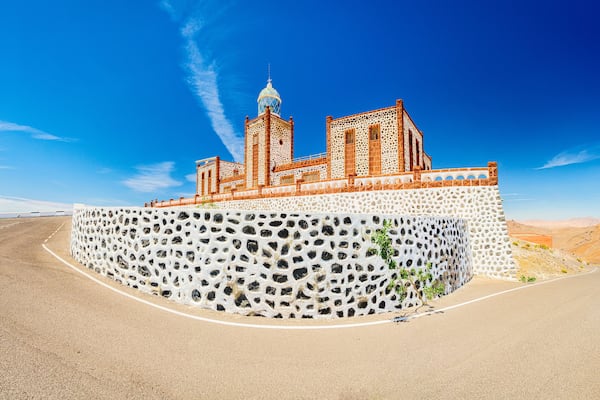 Um edifício grande e ornamentado, com uma cúpula e várias torres, localizado em um afloramento rochoso sob um céu azul límpido.