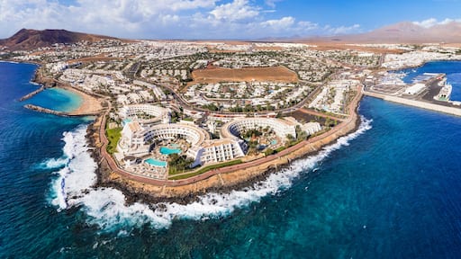 An aerial view of a coastal resort with a large pool, beachfront villas, and a marina.