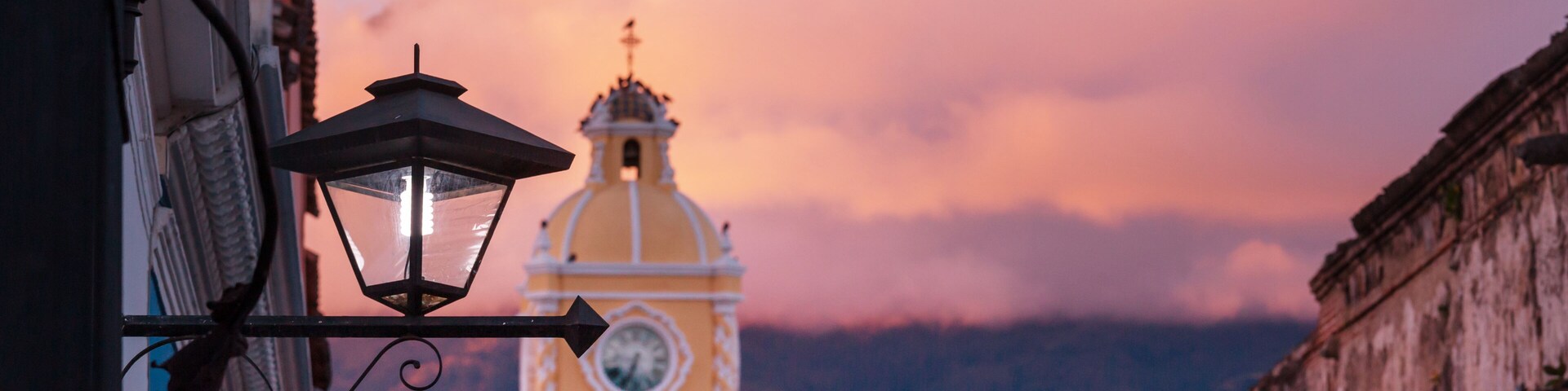 Un edificio amarillo con una torre de reloj y una montaña al fondo.