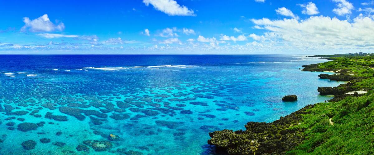 A coastal landscape with clear blue waters, visible coral reefs, and lush greenery.