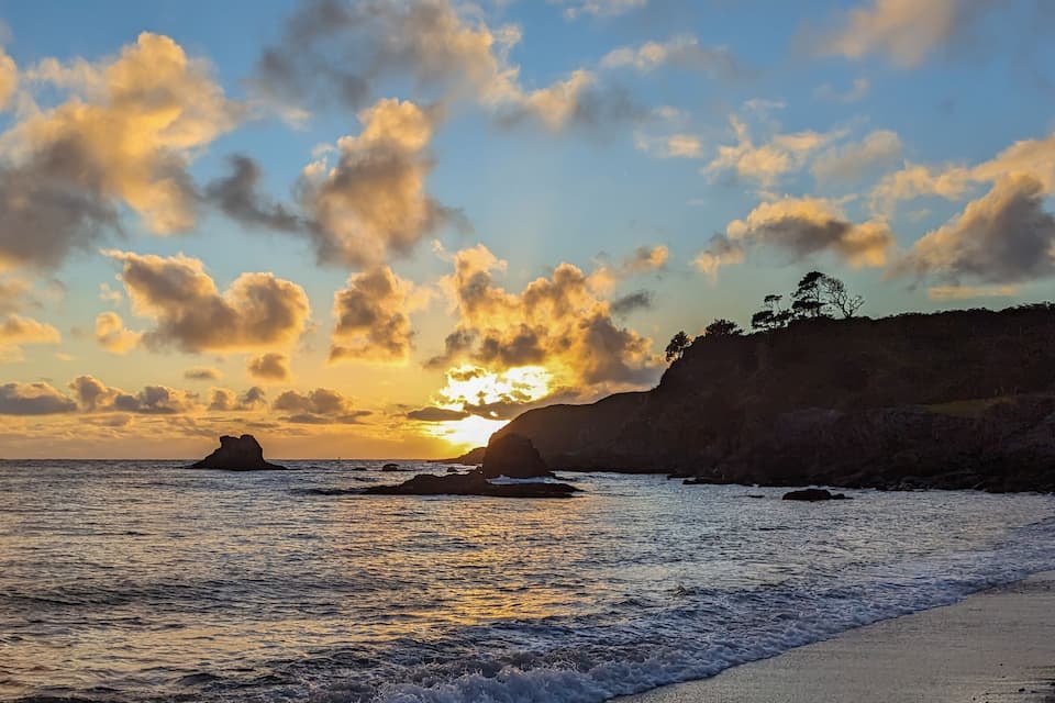 Un atardecer sobre un paisaje costero con acantilados rocosos y una playa de arena.