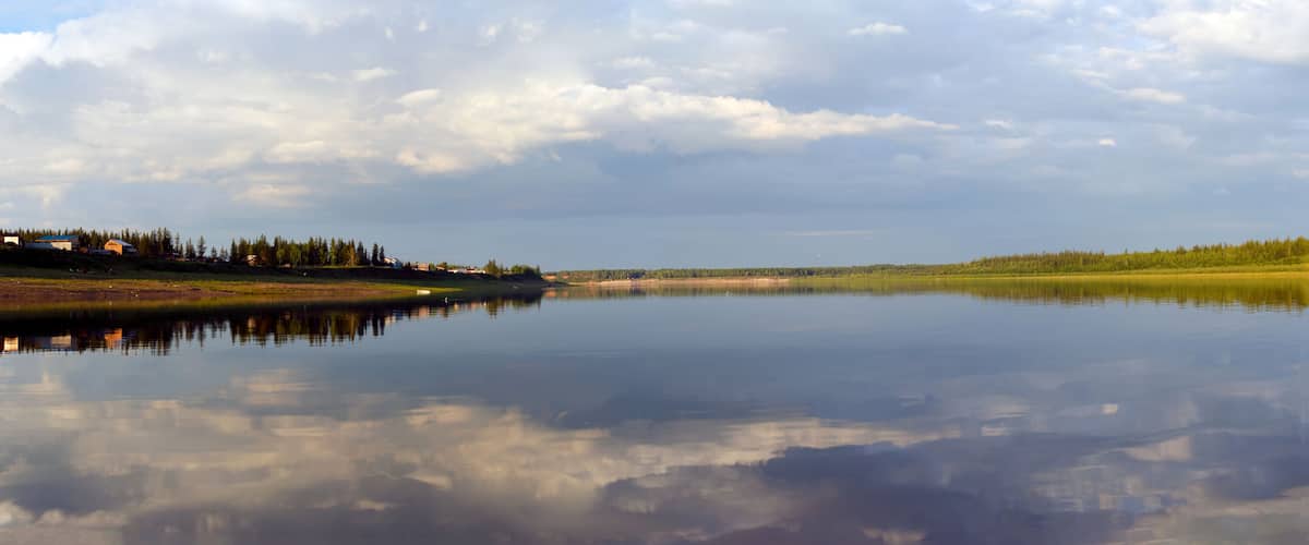 Bright reflection of the sky and banks in the Northern river vilyu in Yakutia at sunset in the evening in the spruce forest and the village houses.