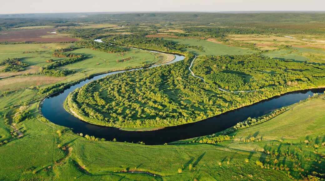 Aerial view of winding Sura river among green plains and forest trees on a summer sunny evening. Natural environment of Central Russia in Penza region