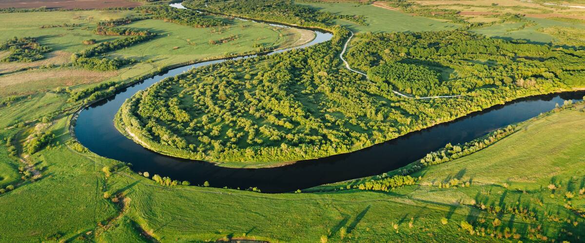 Aerial view of winding Sura river among green plains and forest trees on a summer sunny evening. Natural environment of Central Russia in Penza region