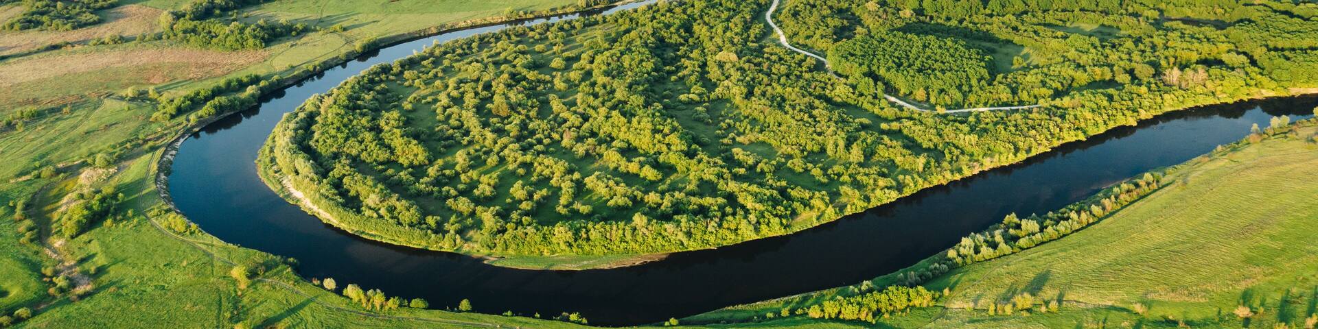 Aerial view of winding Sura river among green plains and forest trees on a summer sunny evening. Natural environment of Central Russia in Penza region