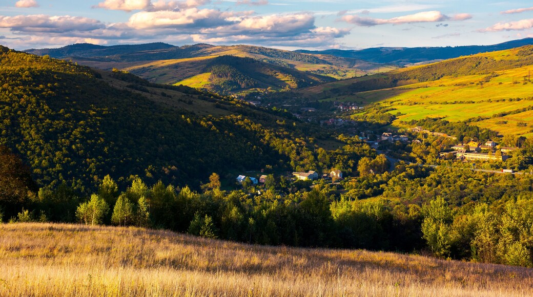 beautiful Carpathian countryside at sunset. village down in the valley in shade of a nearby mountain. beautiful colorful sky with clouds. Great water dividing ridge in the far distance