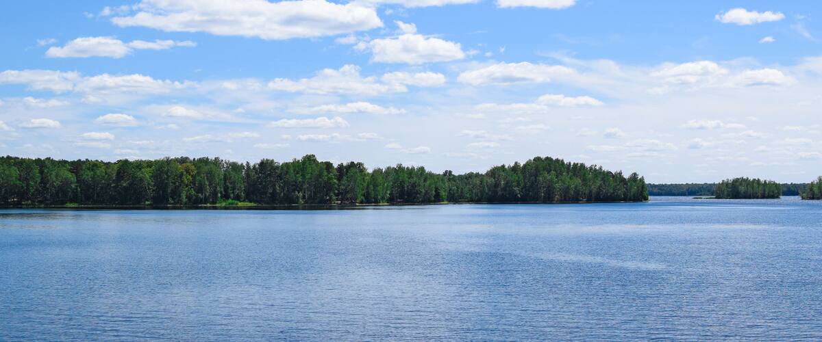 Beautiful summer landscape. Bright blue sky, white clouds, lake, forest.