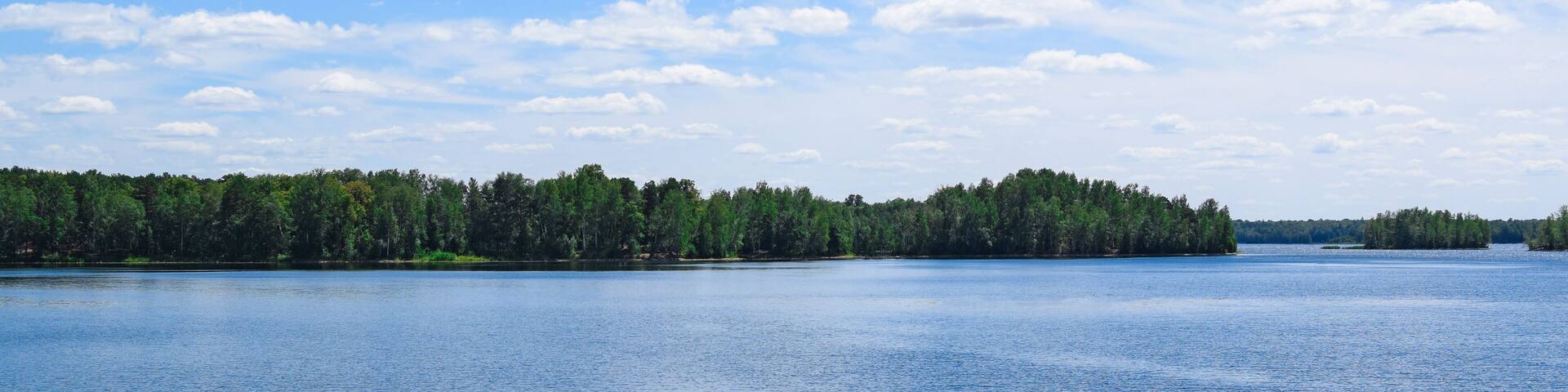 Beautiful summer landscape. Bright blue sky, white clouds, lake, forest.