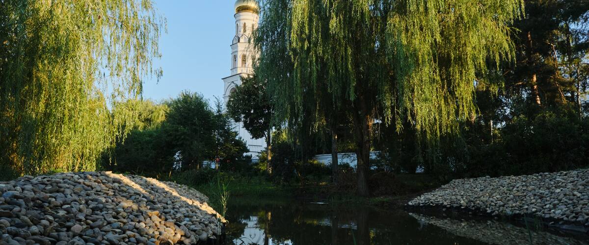 A beautiful tall white Christian building with a golden dome and a cross. A small lake in the park nearby. Convent of the Icon of the Mother of God, Dinskoy district Krasnodar, south of Russia.
