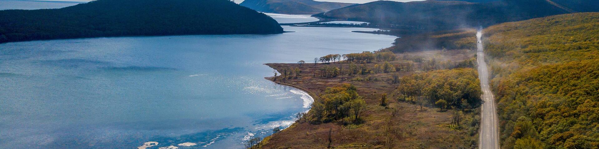 The road passes next to a large lake in a dense forest in summer. View from above. Large lagoon lake. The nature of the Primorsky region.