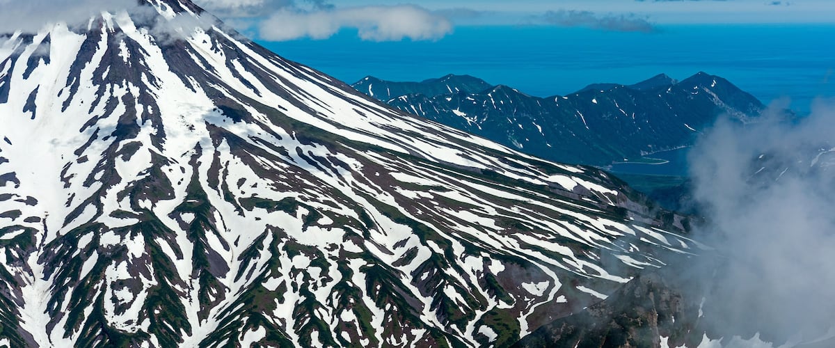 Aerial view of snowcapped Vilyuchinsk Volcano surrounded by clouds and a breathtaking landscape, Kamchatka Peninsula, Russia.