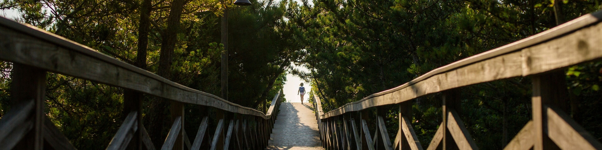 A small child is silhouetted in the distance at end of long boardwalk